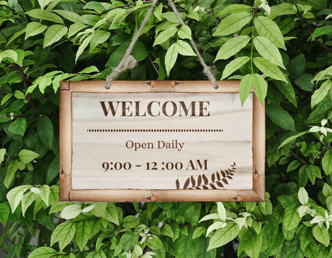 Hanging bamboo wooden welcome sign displayed among green leaves.
