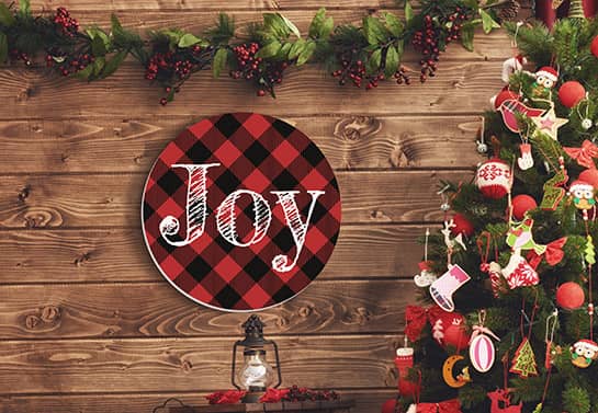 Buffalo plaid Christmas sign mounted on a wall that spells the word JOY
