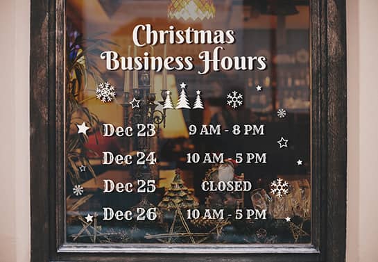 Christmas sign displaying the holiday business hours adhered to a storefront window