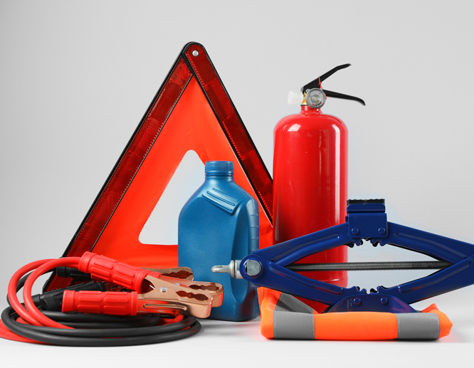 Car emergency kit with a reflective warning triangle, fire extinguisher, jumper cables, and other roadside safety tools.