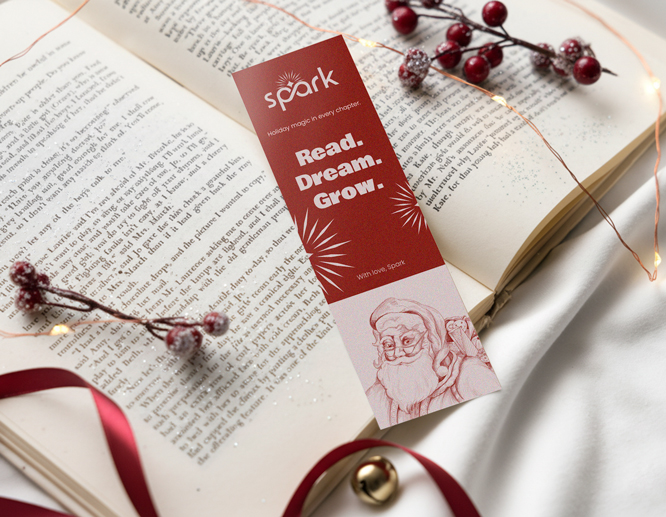 Spark bookmark reading 'Read. Dream. Give.' on open book with holiday decorations.
