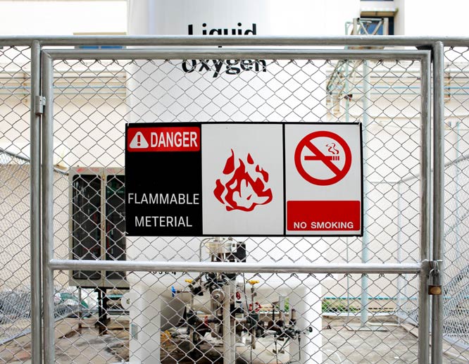 Safety signs reading flammable and no smoking and displaying a flame icon fixed to a fence.