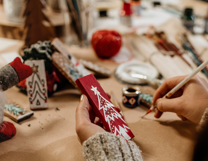Person painting wooden Christmas signs with festive tree and holiday patterns.
