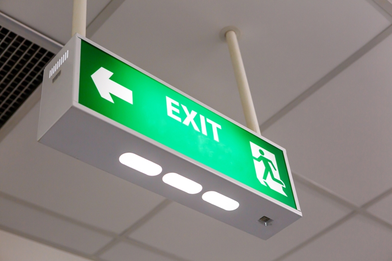 Example of an emergency exit signage in green hanging from the ceiling with a directional arrow