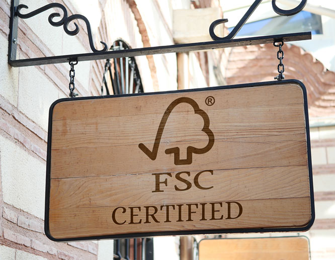 FSC-certified wooden hanging sign mounted on a metal bracket outside a building.