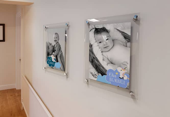 Child’s photos hung in a row on a long hallway wall displaying a Our big miracle note