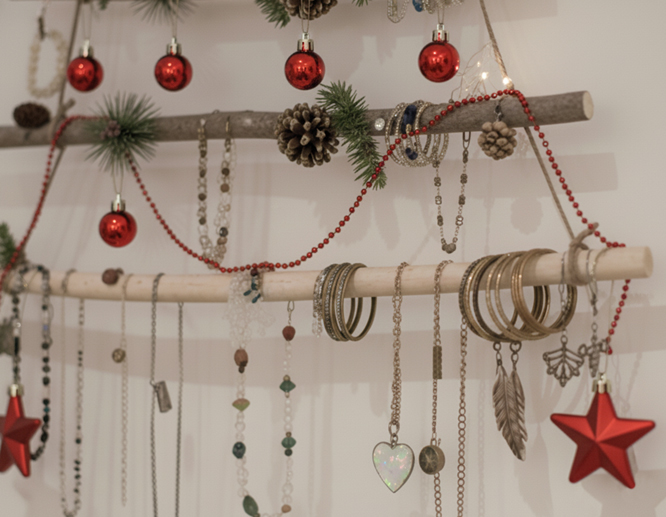 Fancy jewelry hanging from a wall-mounted wooden Christmas tree, decorated with red Christmas balls, pine cones, and lights