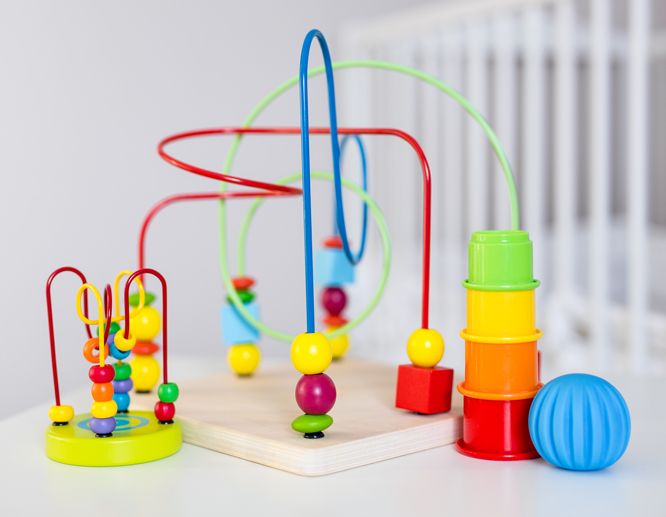 Colorful educational toys including a bead maze, stacking cups, and a textured ball on a nursery table.