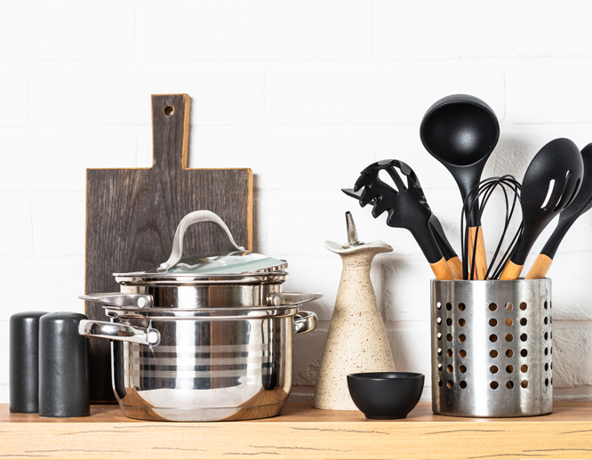 Kitchen essentials including stainless steel pots, cooking utensils, cutting boards, and an oil dispenser on a wooden counter.