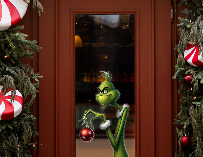 A Christmas window decal displays the Grinch grinning and holding a red Christmas ball