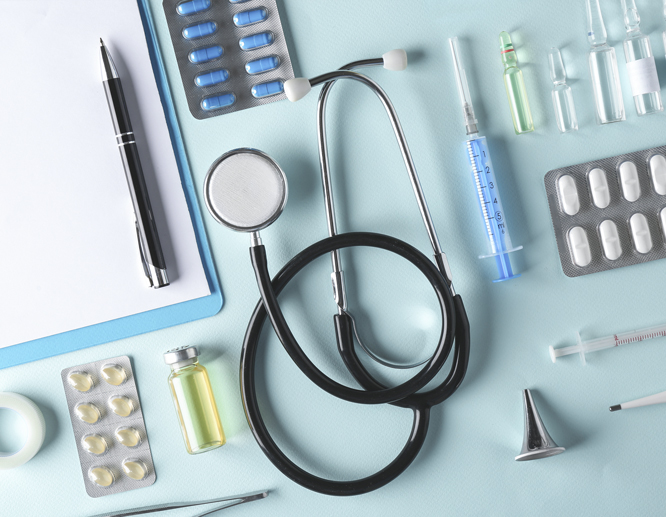 Flat lay of medical supplies featuring a stethoscope, syringe, blister packs, and vials on a light blue background.