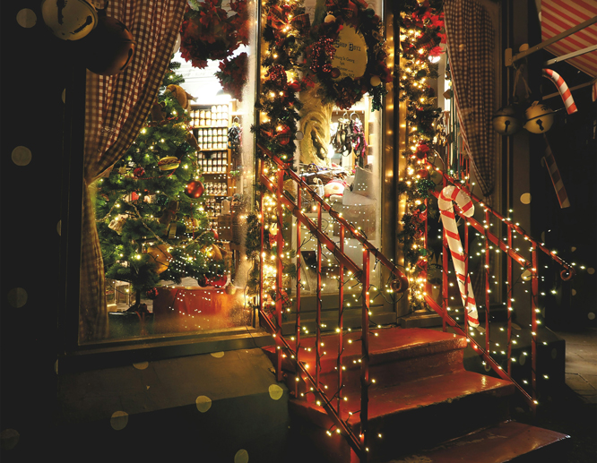A storefront decorated with lots of festive Christmas lights and a wreath hanging from the main door