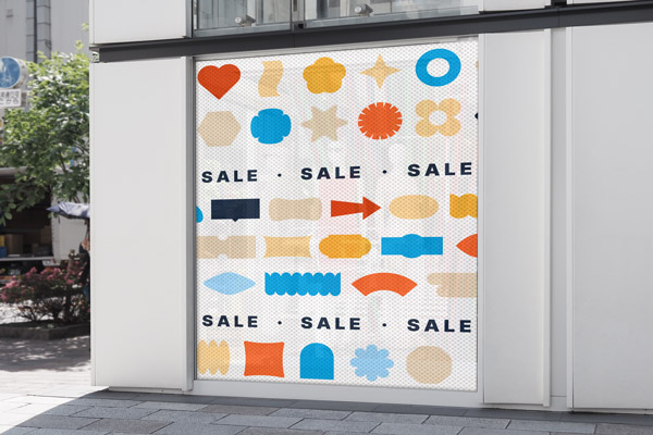 A colorful perforated window decal on a storefront highlighting promotional sales the store is running.