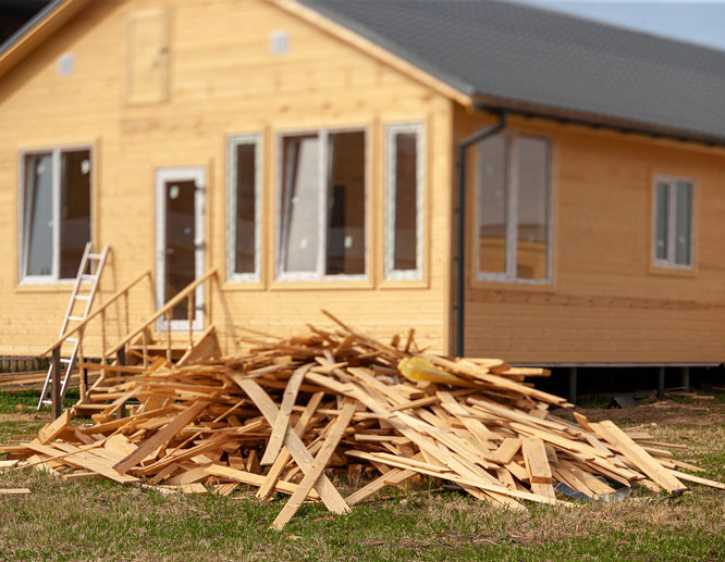 Pile of reclaimed wood planks in front of a wooden house under construction.