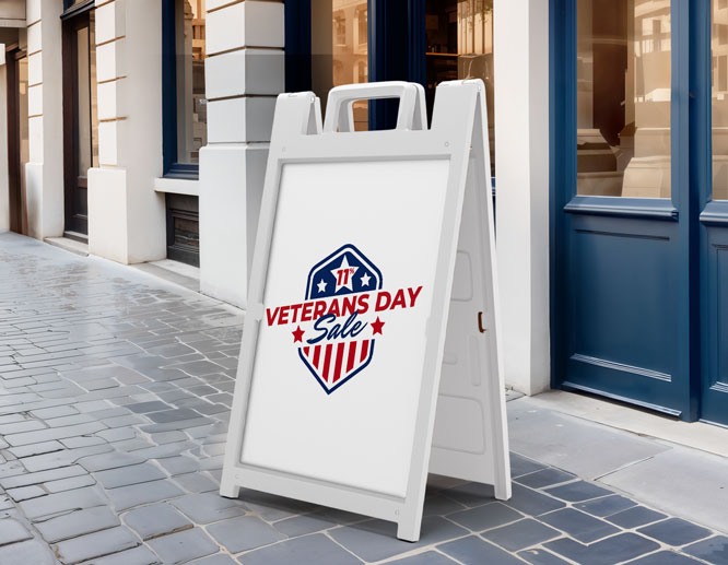 A-frame sidewalk sign promoting Veterans Day Sale with patriotic red, white, and blue shield design outside a store.