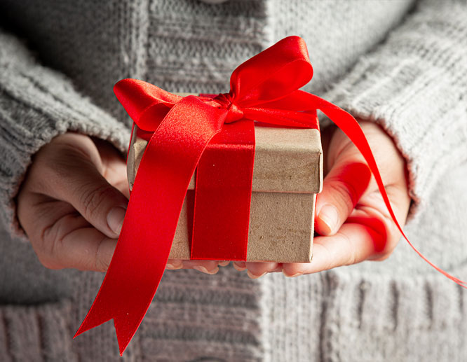 Person in gray sweater holding a small gift wrapped with red ribbon, symbolizing customer appreciation holiday gifts.