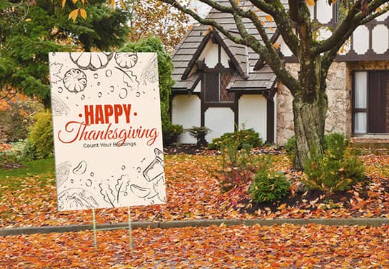 beige Thanksgiving yard sign surrounded by autumn leaves