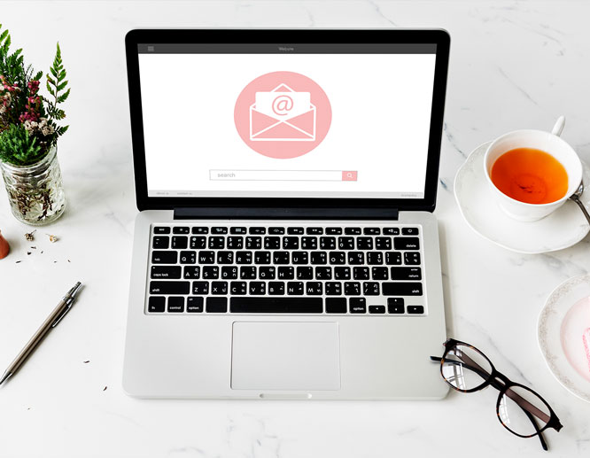 Laptop on desk with email icon on screen, cup of tea, and glasses nearby, representing fall direct mail and email marketing ideas.