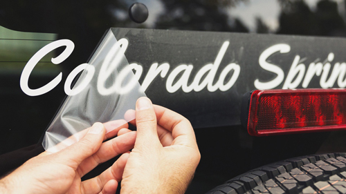 Hands applying white lettering custom car window decal on vehicle glass