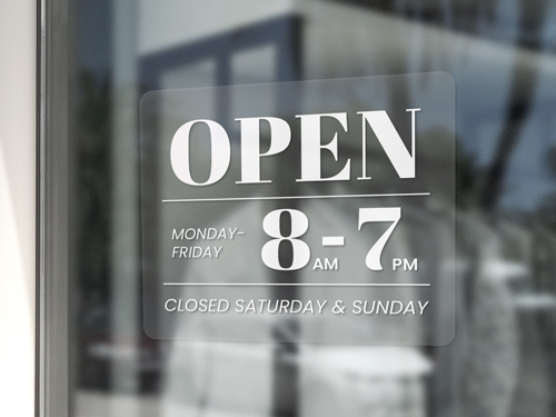 A clear window cling showcasing a shop's working hours in white letters.